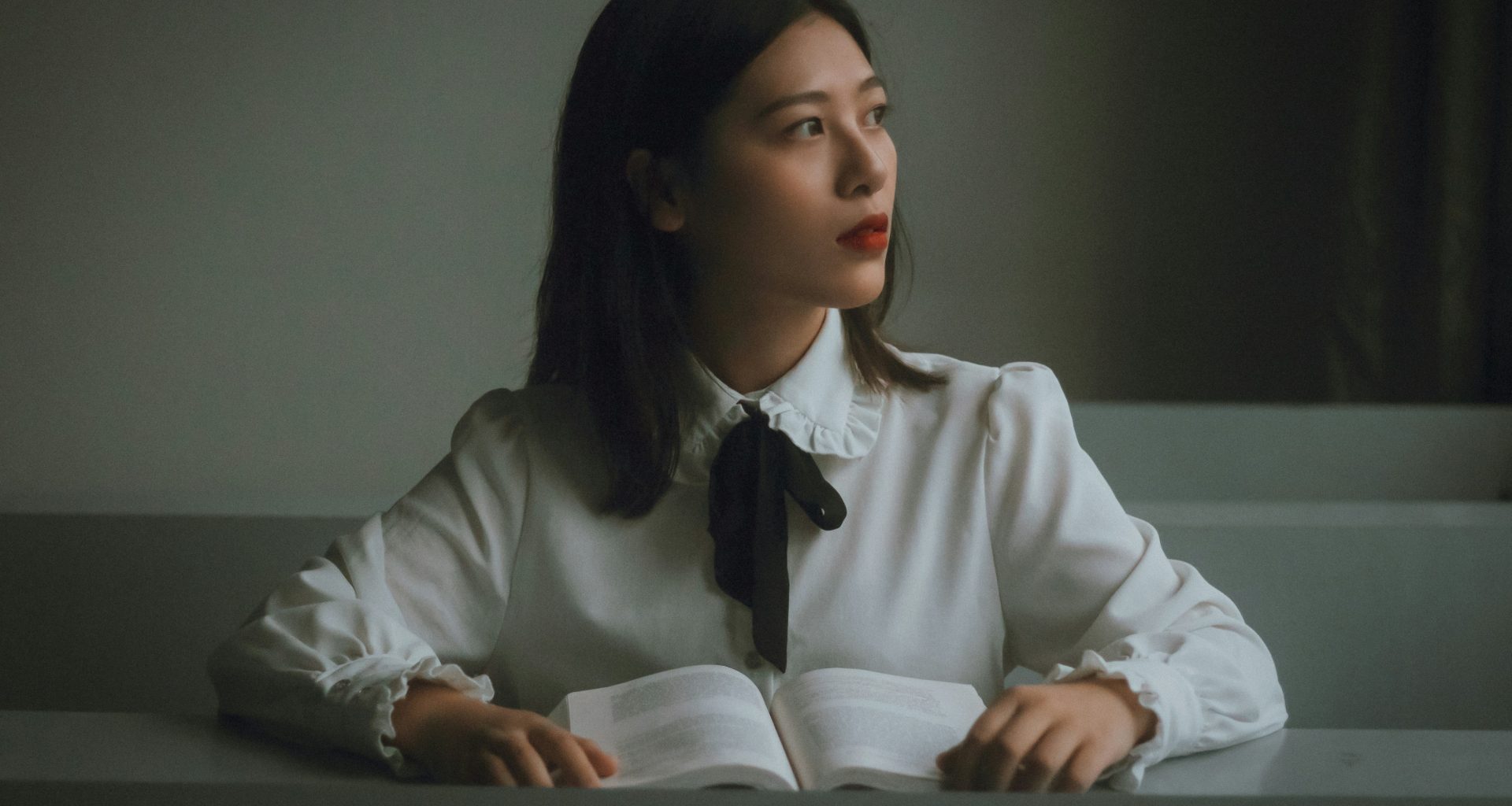 eine-frau-sitzt-an-einem-tisch-mit-einem-aufgeschlagenen-buch-aet4XLxrKpc