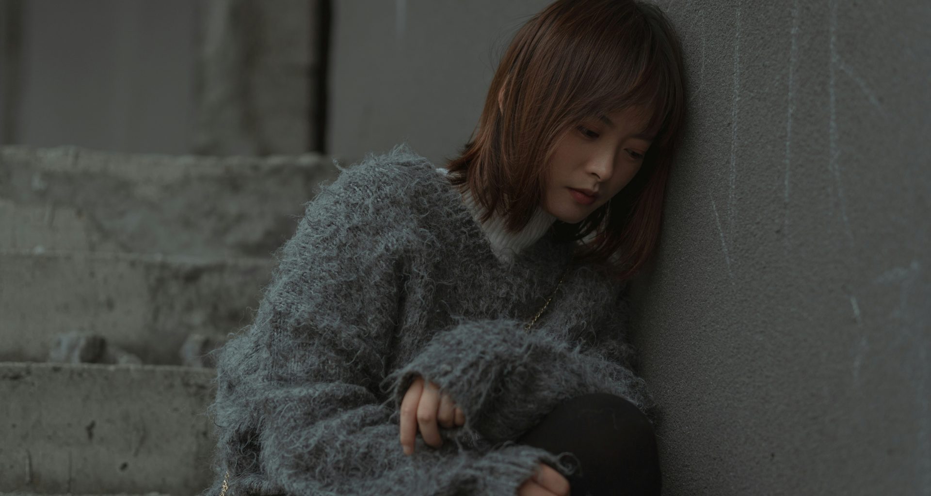 frau-im-grauen-pullover-sitzt-auf-grauer-betonbank-TncCMk2dQeQ
