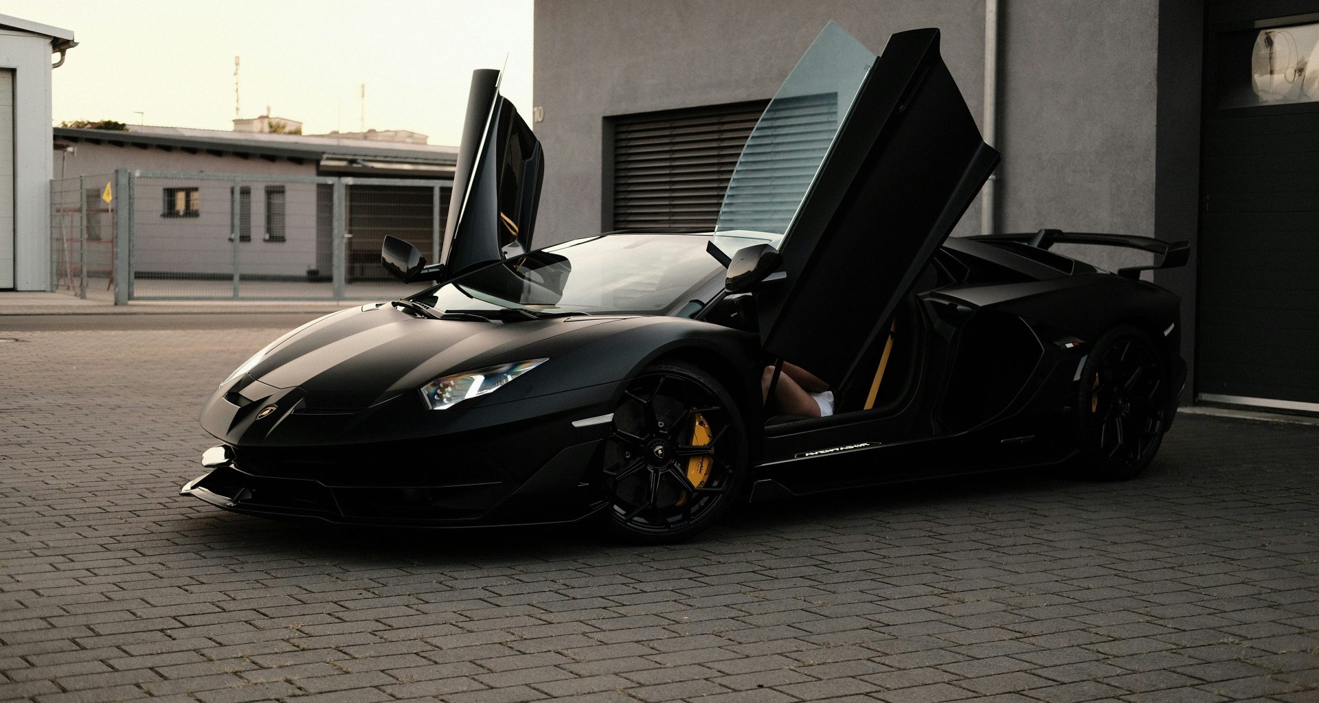 ein-schwarzer-sportwagen-der-vor-einer-garage-geparkt-ist-pSYNs4xFACc