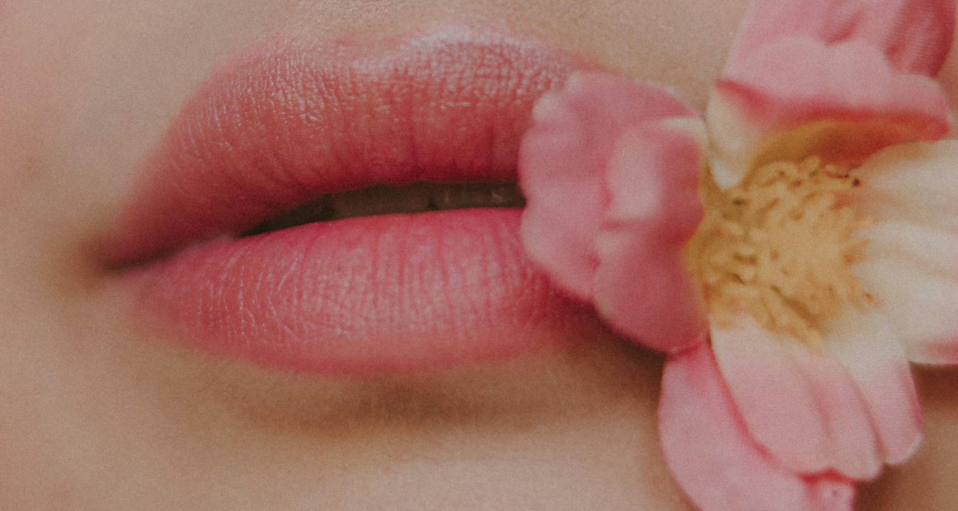 eine-nahaufnahme-der-lippen-einer-frau-mit-einer-blume-im-mund-RnuIAWvlHBw