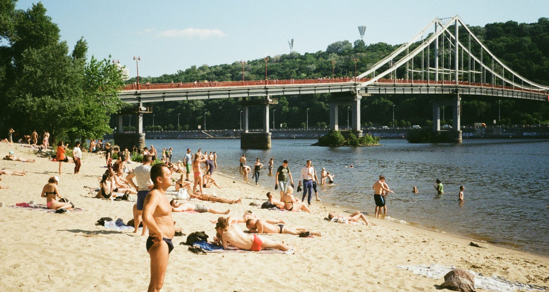 eine-gruppe-von-menschen-an-einem-strand-in-der-nahe-einer-brucke-88DWugInbA4