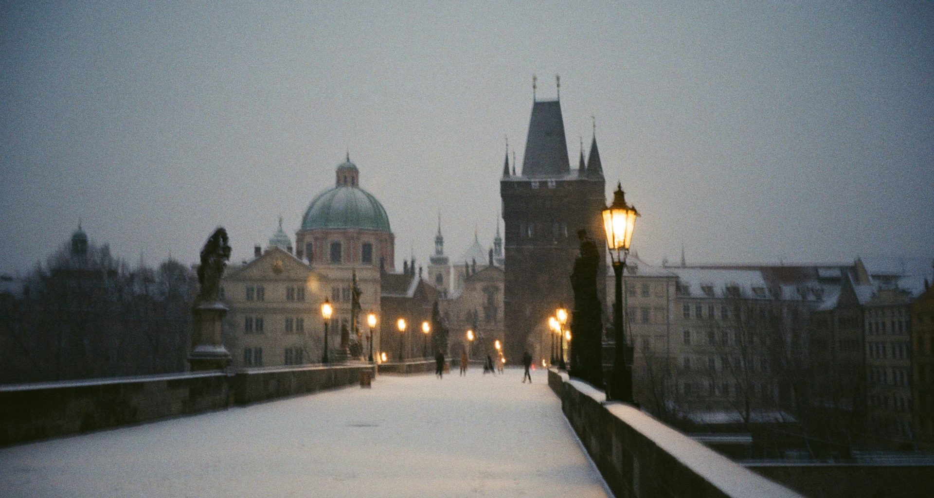 ein-verschneiter-gehweg-mit-einer-strassenlaterne-und-gebauden-im-hintergrund-0aDCezTFkVU