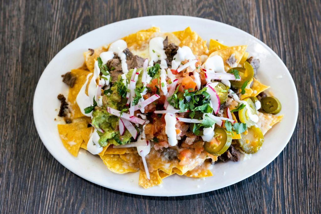 ein-weisser-teller-mit-nachos-die-mit-toppings-uberzogen-sind-F1THVKiumJY