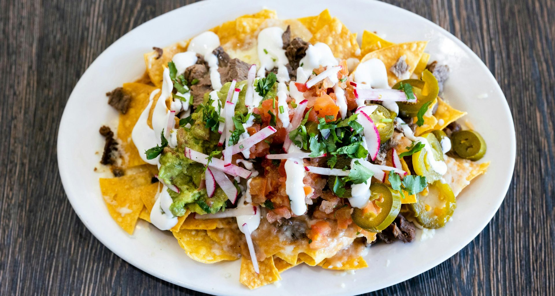 ein-weisser-teller-mit-nachos-die-mit-toppings-uberzogen-sind-F1THVKiumJY