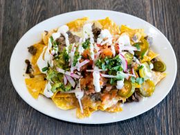 ein-weisser-teller-mit-nachos-die-mit-toppings-uberzogen-sind-F1THVKiumJY