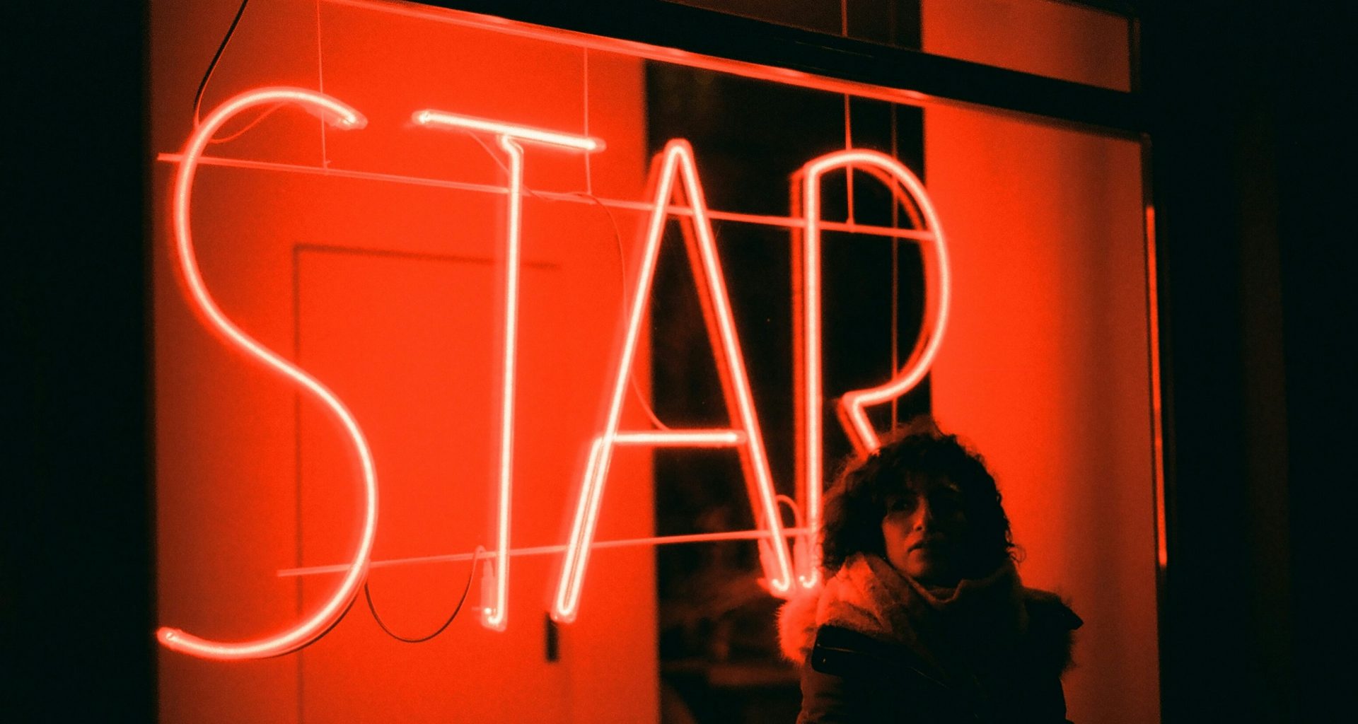 eine-frau-steht-vor-einer-leuchtreklame-9-oNehIJqRY