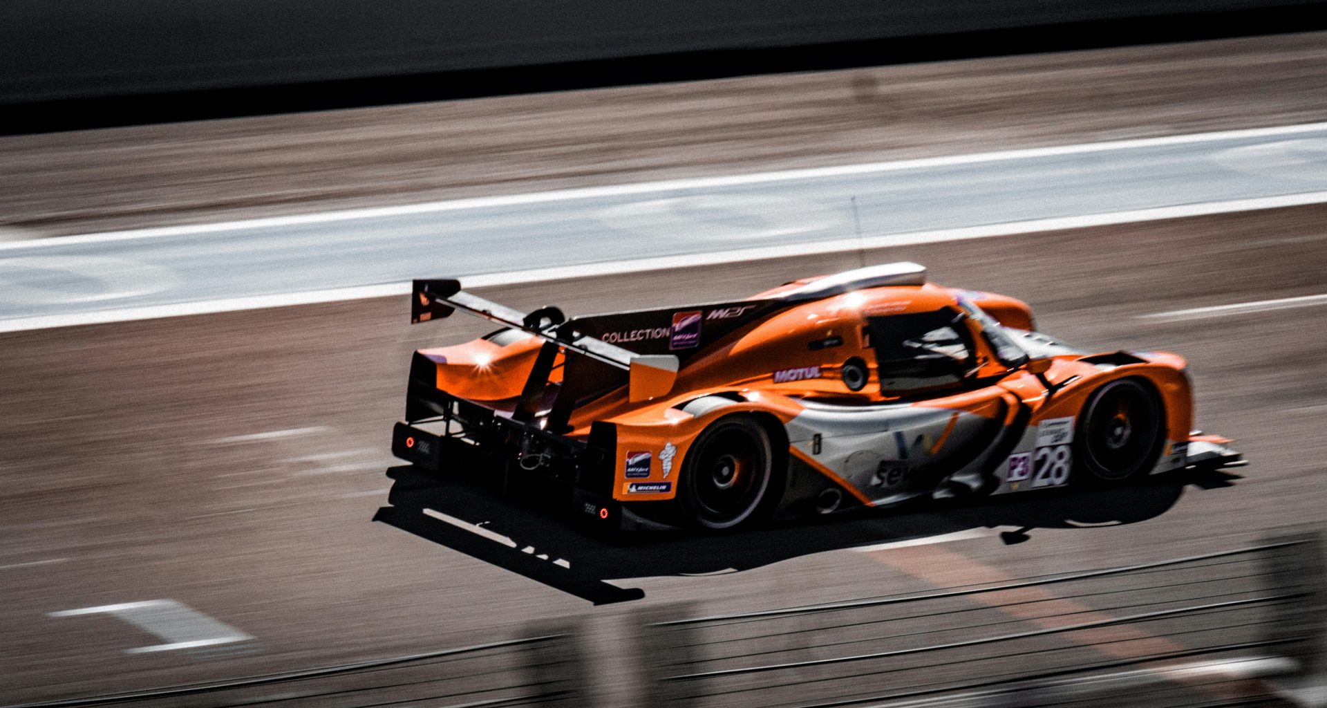 ein-orangefarbener-rennwagen-fahrt-eine-rennstrecke-hinunter-NJ14CfJwwtI