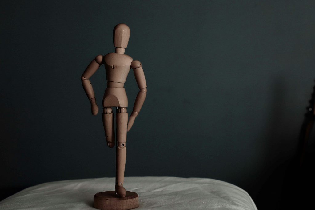 braune-menschliche-holzfigur-auf-weissem-textil-iHnWBtpYMEc