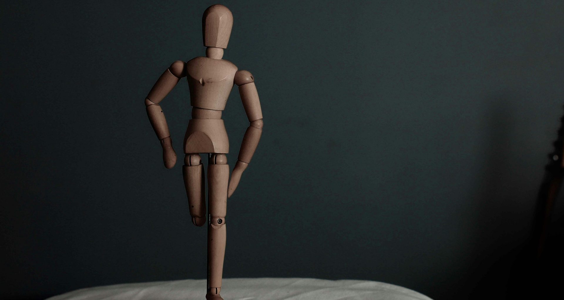 braune-menschliche-holzfigur-auf-weissem-textil-iHnWBtpYMEc