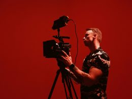 mann-in-schwarz-weissem-rundhals-t-shirt-stehend-und-mit-schwarzer-kamera-jvu8vJIMtjw