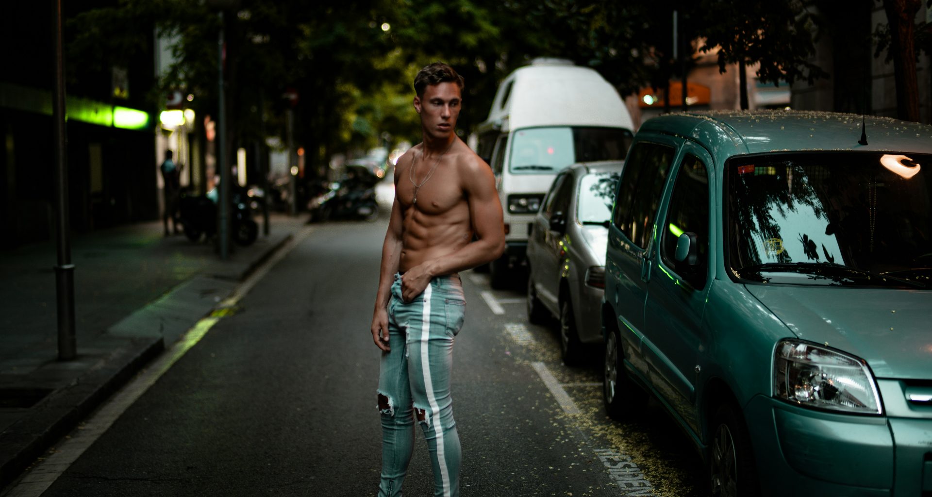 mann-in-blauer-amiri-denim-trainingshose-steht-neben-grunem-auto-R6RzTNFz3ms