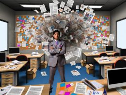 Frustrierter Marketer inmitten eines unorganisierten Büros mit verstreuten Dokumenten, digitalen Geräten und kreativer Unordnung