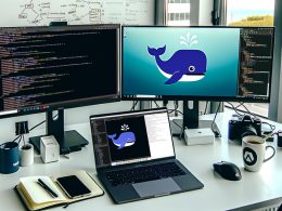 Minimalistischer Entwicklerarbeitsplatz mit Laptop, auf dem ein Dockerfile in VS Code geöffnet ist, externer Monitor mit Docker Whale-Logo, lokalen App-Fenstern, Notizbuch, Kaffee und moderner Technik.