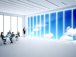 Modernes Büro ohne echte Fenster mit LED-Panels, die realistischen Himmel und Wolken zeigen. Mitarbeitende arbeiten an Laptops in einer lichtdurchfluteten, innovativen Umgebung.