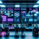 Futuristisches Data-Operations-Center mit neonfarbenen Datenströmen, Kontrollwand, Data Engineers vor Glasbildschirmen und digital schwebenden Symbolen im Jahr 2025.