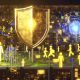 Goldenes Amazon Ads-Logo über digitalen Serverstädten, KI-Schutzschild erkennt und blockiert Bots, während Klickfarmen digitale Goldströme erzeugen.