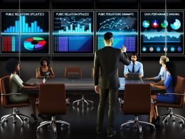Team von PR-Spezialisten analysiert bunte Datenvisualisierungen auf großen Bildschirmen in einem modernen Büro, während ein Manager Einsichten präsentiert.