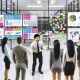 Dynamisches Team präsentiert und analysiert verschiedene bunte Datenvisualisierungen an großen Bildschirmen in einem modernen, energiegeladenen Büro mit Glaswänden und Whiteboards.