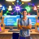 SEO-Experte an einem Schreibtisch mit mehreren Monitoren zeigt kostenlose SEO-Tools wie Google Search Console, Ubersuggest, Ahrefs Free Tools und Screaming Frog, davor bunte digitale Werkzeugkoffer, im Hintergrund Premium-Suites mit Preisschildern.