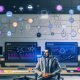 Person in modernem Büro vor Monitoren mit Dashboards, schwebenden API-Icons und Diagrammen, die smarte Automatisierung und Webflow Reporting symbolisieren.