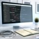 Minimalistischer Arbeitsplatz mit großem Monitor, darauf Webflow-Interface und geöffneter CSS-Klassenübersicht, dazu ein technisches Notizbuch mit Checkliste.
