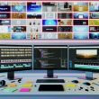 Moderner Arbeitsplatz mit mehreren Bildschirmen für automatisierte Videobearbeitung, Code und Social Media Analytics, umgeben von Technik-Accessoires und auffälligen Video-Thumbnails an der Wand.