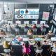 Vogelperspektive auf ein modernes PR-Büro mit mehreren Expert:innen, die an Laptops und großen Monitoren mit Dashboards, Medienmonitoring und Pressemitteilungen arbeiten.