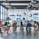 Helles Großraumbüro mit modernen Arbeitsplätzen, mehreren Monitoren mit Datenanalysen und Social-Media-Feeds, PR-Expert:innen im Gespräch, digitales Dashboard und Leinwand mit Artikel-Headline im Vordergrund.