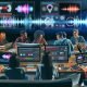 Junge Content-Creator diskutieren an Laptops und Monitoren über Videoclips, Trending Audios und Datencharts aus Social-Media-Apps wie TikTok, YouTube Shorts und Instagram Reels in einer modernen Marketing-Umgebung.