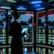Futuristischer IT-Kontrollraum im Halbdunkel mit moderner Person vor Monitoren, die Cybersicherheits-Bedrohungen und Warnhinweise anzeigen. Verschwommene Serverracks und digitale Linien im Hintergrund erzeugen eine angespannte Atmosphäre.