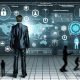 Geschäftsmann im Anzug bedient holografisches Sicherheits-Dashboard vor digitaler Wand mit Datenströmen, Firewalls, Überwachung und Schutzsymbolen in einem hochmodernen Büro, während Cyberbedrohungen abgewehrt werden.