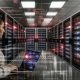 Düsterer Serverraum mit alarmierenden roten Lichtern, digitaler Sicherheitsüberlagerung, professioneller Person am Laptop und Datenströmen im Vordergrund.