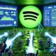 Futuristische digitale Kampfszene mit übergroßem Spotify-Logo, Roboterhänden, geisterhaften Bots, Werbetafeln und KI-Systemen in einem neonbeleuchteten Raum.