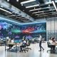 Junges, diverses Team arbeitet kollaborativ an großen interaktiven Bildschirmen voller farbenfroher Datenvisualisierungen, umgeben von einer innovativen Atmosphäre und Echtzeit-Daten an der digitalen Wand.