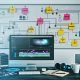 Moderner, organisierter Video-Editing-Arbeitsplatz mit Monitor, Notizen zur Themenplanung, Skripterstellung und Asset-Management sowie digitalen Symbolen für Zusammenarbeit und Dateiorganisation.