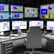 Futuristischer Büroarbeitsplatz mit mehreren Bildschirmen voller SEO-Analytics, Keyword-Tools und Rankings, strukturierter Schreibtisch mit Notizen und Checklisten, große bunte Website im Hintergrund zwischen verschwimmenden Konkurrenzseiten.