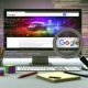 Computer-Bildschirm mit leuchtenden, individuellen Bildern, umgeben von technischen Notizen, Stift und Symbolen für Bildsuche. Dezente Hinweise auf Web-Code und moderne Bildformate, Stockfoto im Hintergrund.