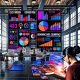 Team für digitales Marketing analysiert Performance-Metriken auf großen, farbenfrohen Dashboards in offenem Loft-Büro, vorn ein Marketer mit Notebook