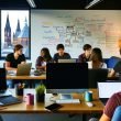 Junge Fachleute arbeiten in einer kreativen Büroumgebung in Mainz an Laptops, mit Whiteboard voller SEO-Diagramme und Blick auf den Mainzer Dom.