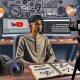 YouTube-Creator sitzt im Home-Office an Monitoren mit Videobearbeitung, Affiliate- & Analytics-Tools, Notizbuch mit Keywords und Kameraequipment im Hintergrund.