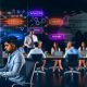 Fokussierter SEO-Spezialist vor Monitoren mit Analytics- und SEO-Tools, umgeben von Notizen und Diagrammen, im modernen Büro mit Team und digitalen Keywords wie Technical SEO, Content, Backlinks und Strategy.
