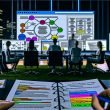 Modernes Büro bei Nacht mit mehreren Menschen in angespannter Gruppendiskussion vor großer Bildschirmfläche, die komplexe Website-Architektur und SEO-Daten zeigt. Im Vordergrund ein SEO-Notizblock, im Hintergrund Monitore mit Tools wie Screaming Frog.