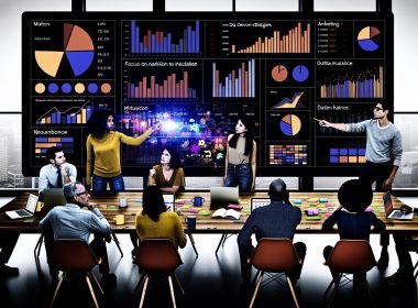 Marketingteam diskutiert vor digitalem Dashboard mit bunten Grafiken und Marketingkennzahlen im modernen Büro, während der Teamleiter auf Analysen hinweist.