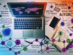 Moderner Schreibtisch aus der Vogelperspektive mit offenem Laptop, Smartphone mit Social Media-Apps, handgeschriebenen Notizen, bunten Infografiken, SEO-Diagrammen und Symbolen für Netzwerkaufbau und Reichweite.