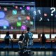 Gestresster Marketing-Manager vor digitalen Dashboards mit verworrenen Kanälen und skeptischem Chef im Büro bei Dämmerung.