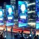 Dynamische, futuristische Stadt bei Nacht mit leuchtenden Bildschirmen, auf denen KI-Avatare in animierten Chatfenstern interagieren, während Menschen im Vordergrund an digitalen Geräten Gespräche führen.