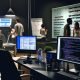 IT-Profis arbeiten in einem modernen, sachlich ausgeleuchteten Büro an Monitore mit SEO-Tools und Code, während im Hintergrund Fachleute diskutieren und Messdaten analysieren.