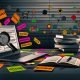 Modernes Homeoffice-Setting mit Laptop, offenem Blog-Editor, Checklisten, SEO-Tools, bunten Diagrammen sowie Notizzetteln mit Schlagwörtern, im Hintergrund Suchmaschinen-Symbole und Bücherstapel.