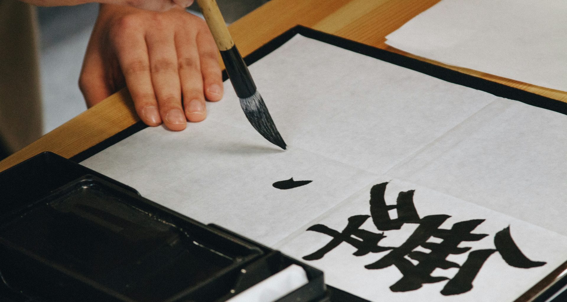 person-mit-schwarzem-pinsel-wahrend-sie-schwarzen-text-auf-weisses-papier-malt-vJqSAasmCEY