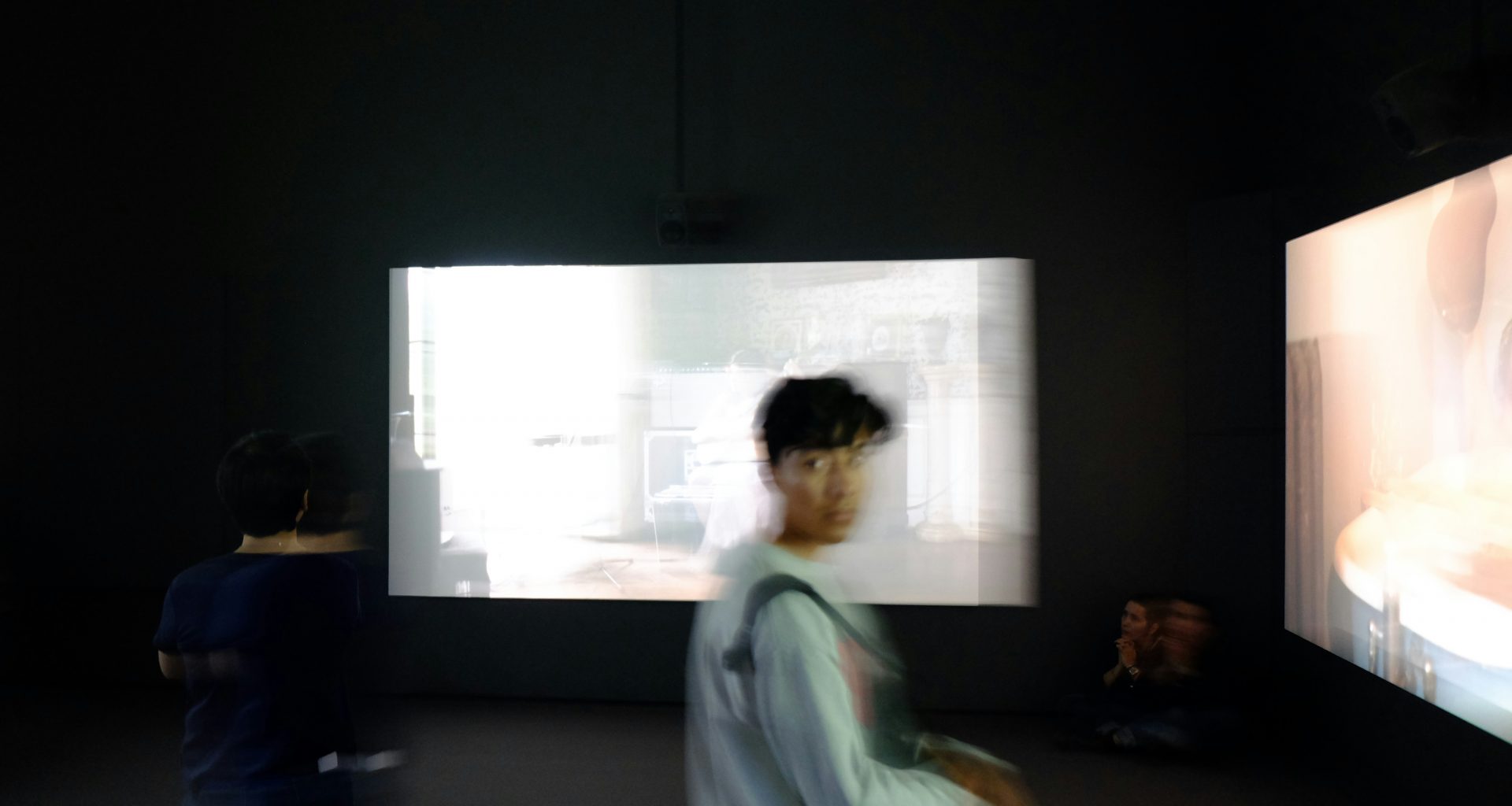 person-im-grauen-pullover-steht-vor-grossen-monitoren-dbOaUuoPXhY